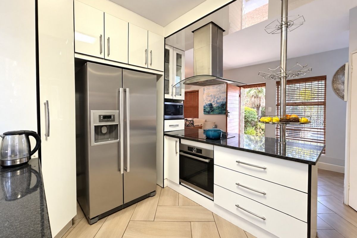 Modern kitchen featuring high-gloss cabinetry, granite countertops, built-in oven, extractor fan, and stylish herringbone tile flooring, seamlessly connecting to the living area.
