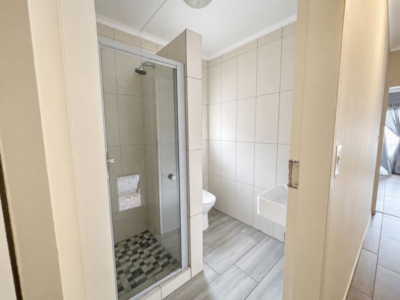 A clean, modern bathroom featuring a glass-enclosed shower, wall-mounted basin, and neutral tiled finishes throughout.