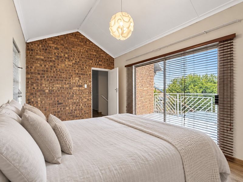 A bright bedroom featuring an exposed brick wall, vaulted ceiling, and large sliding glass doors that open onto a balcony.