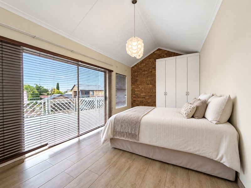 A bright bedroom featuring a vaulted ceiling, exposed brick accent wall, built-in wardrobes, and large sliding glass doors opening to an outdoor balcony.