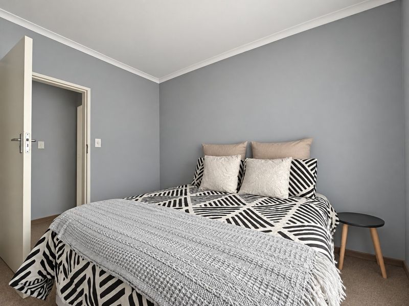 A well-maintained bedroom featuring neutral grey walls, carpeted flooring, and classic coving detail.