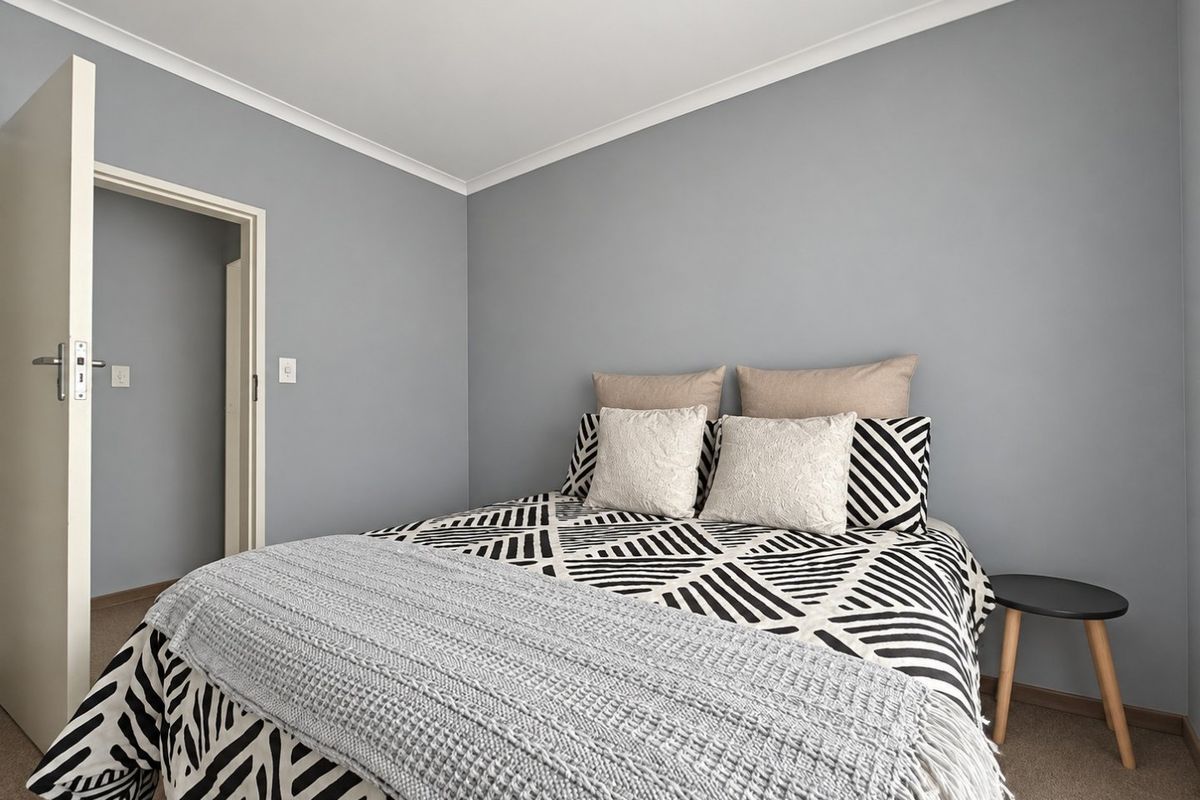 A well-maintained bedroom featuring neutral grey walls, carpeted flooring, and classic coving detail.