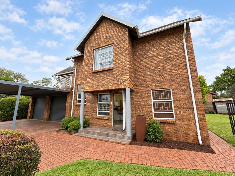 A well-maintained double-story face brick home featuring a paved driveway, double garage, carport, and an upper-level balcony.