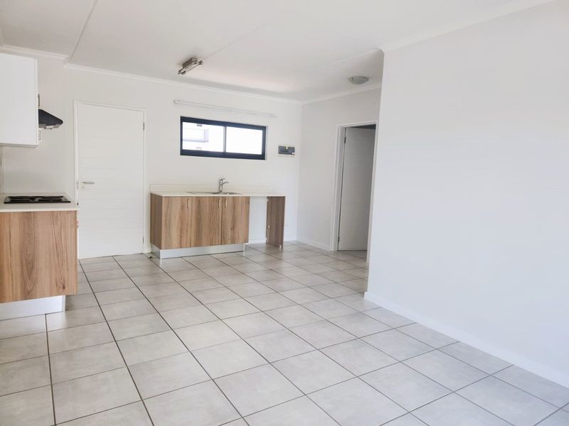 An open-plan living and kitchen area featuring modern wood-finish cabinetry, a gas hob, extractor fan, and neutral tiled flooring throughout.