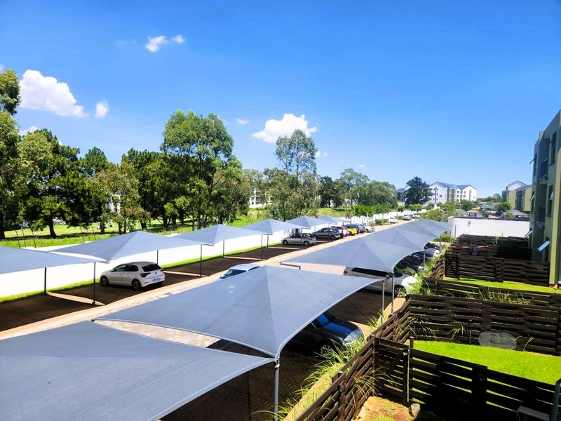 An elevated view of the apartment complex parking area featuring multiple shade cloth carports, paved driveway, and well-maintained timber fencing with lawn.