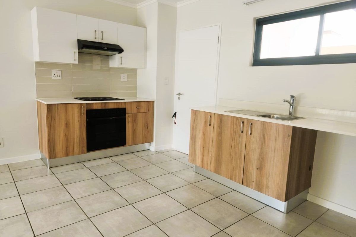 A clean, modern kitchen featuring wood-look cabinetry, white countertops, built-in oven and hob, and neutral tiled flooring in an open-plan layout.