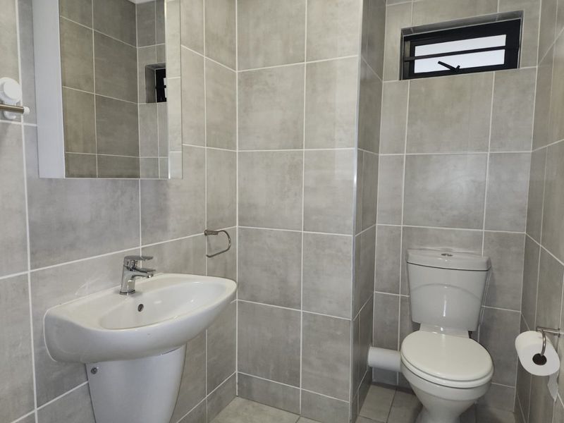 A modern, well-maintained bathroom featuring neutral grey ceramic tiling, a pedestal washbasin, and a standard toilet.