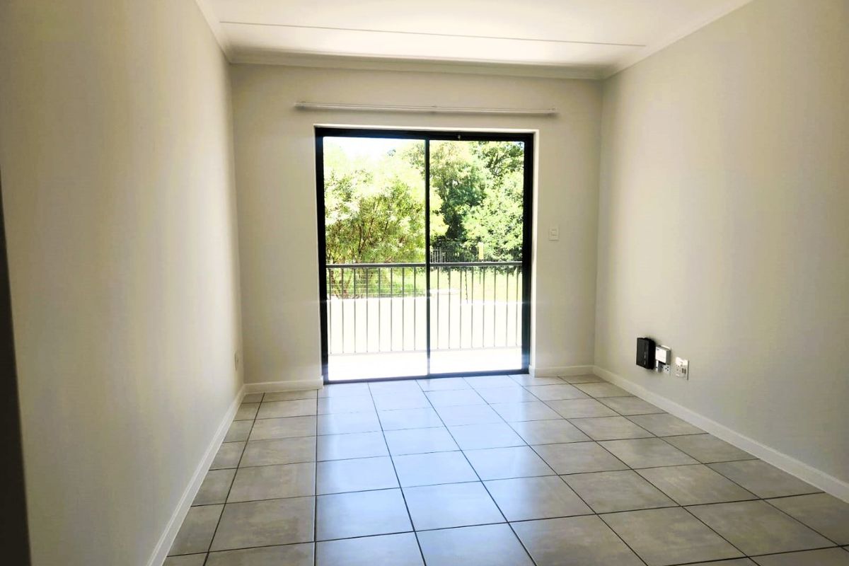 A bright, empty living room featuring neutral tiled flooring and a large sliding glass door that opens onto a balcony with outdoor views.