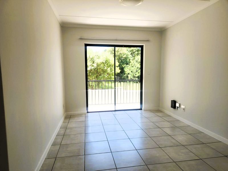 A bright, empty living room featuring neutral tiled flooring and a large sliding glass door that opens onto a balcony with outdoor views.