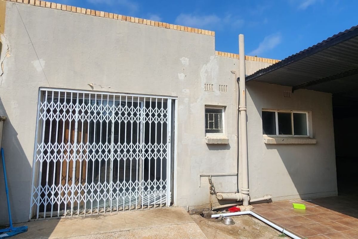 Rear exterior view of the property featuring a tiled patio area, security gate, and sliding door access with visible wear to the exterior wall finish.