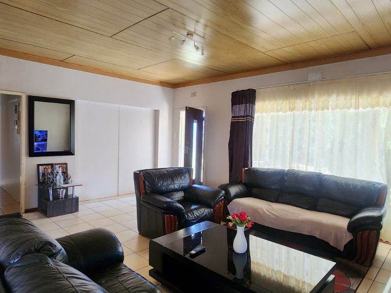 A spacious living room featuring tiled flooring and a timber panelled ceiling, offering a functional layout with natural light from the sliding door.