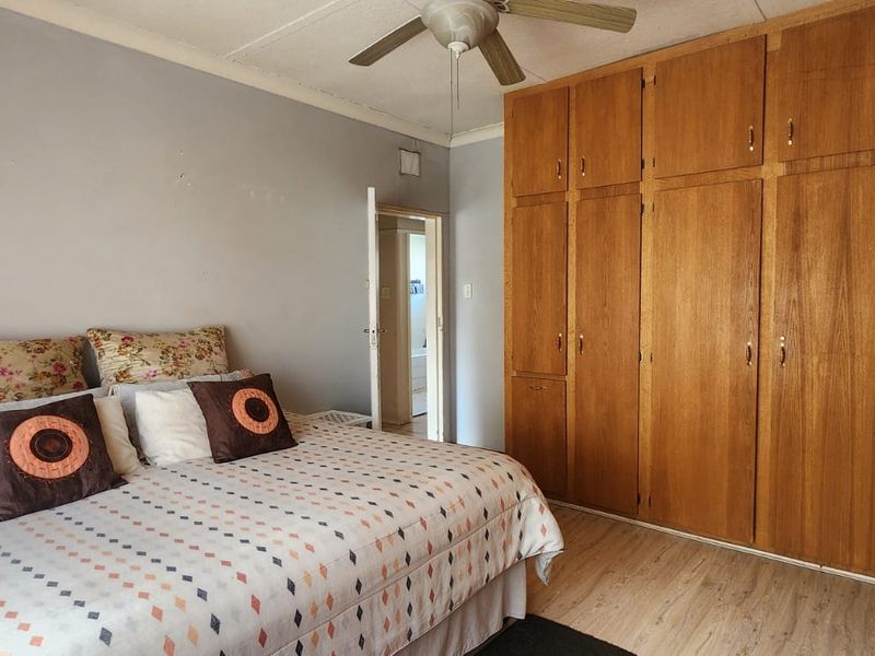 A bedroom featuring laminate flooring, a ceiling fan, and extensive built-in wooden cupboards providing ample storage space.