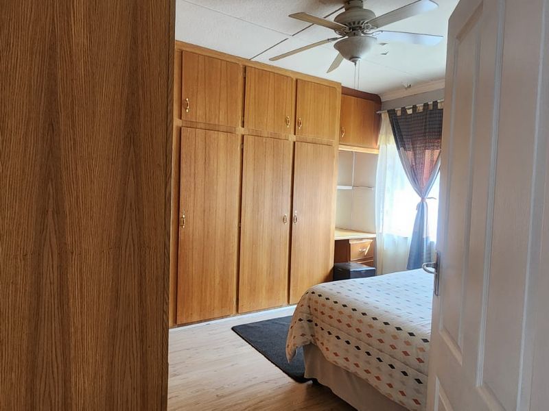 Bedroom featuring extensive built-in wooden cabinetry, a ceiling fan, and light-toned laminate flooring.