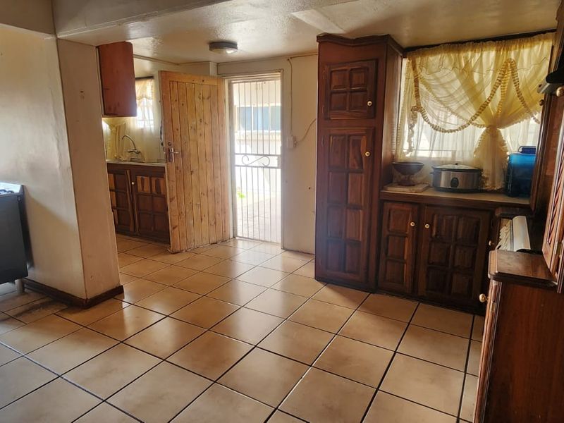 A dated kitchen featuring wooden cabinetry, tiled flooring, and a freestanding gas stove, with direct access to an exterior security gate.