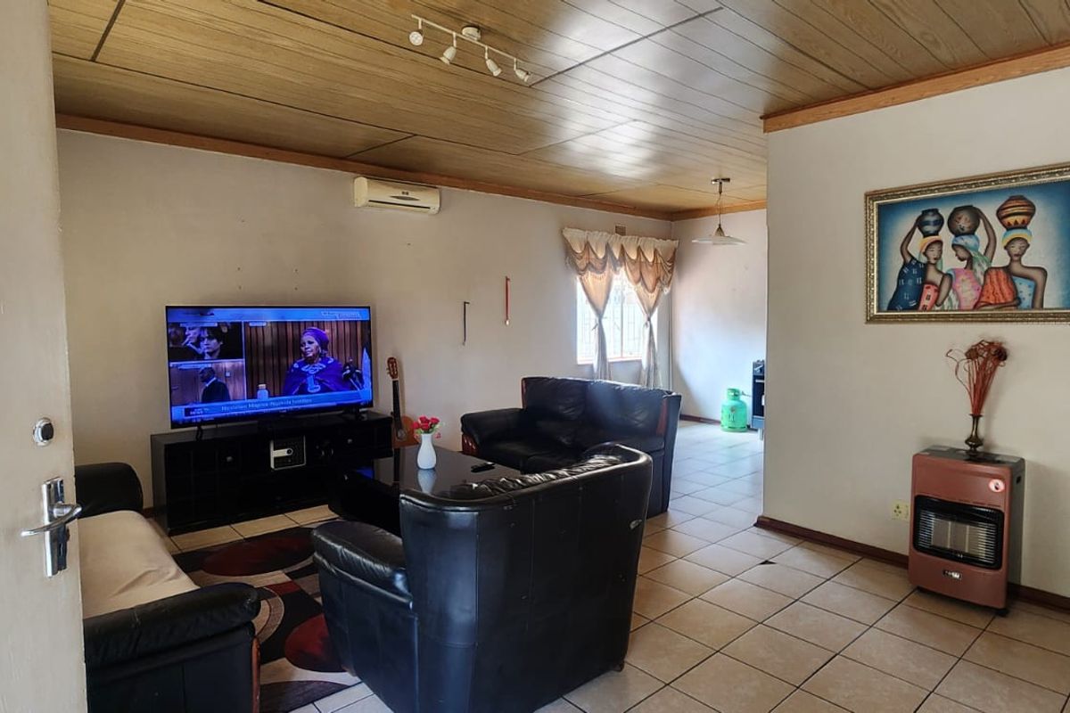 A spacious living room featuring tiled flooring, a wood-paneled ceiling, and a wall-mounted air conditioning unit.
