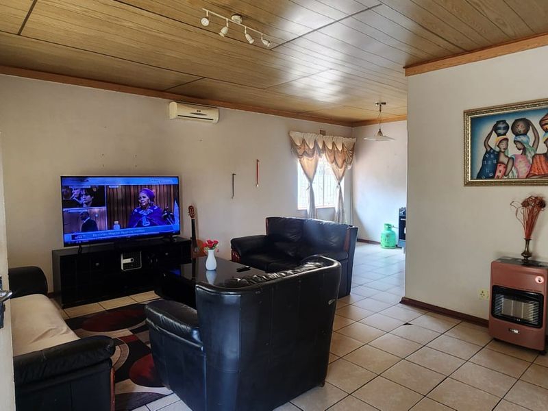 A spacious living room featuring tiled flooring, a wood-paneled ceiling, and a wall-mounted air conditioning unit.