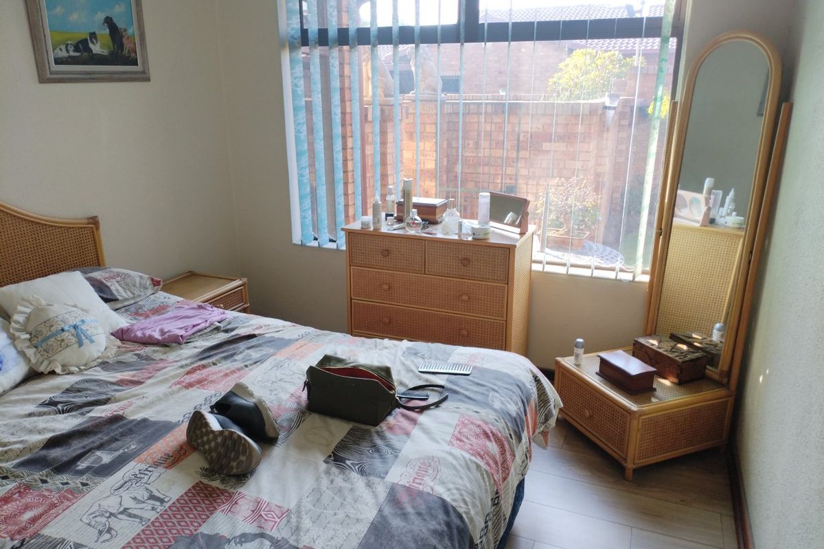 A bedroom featuring laminate flooring and large windows with vertical blinds, offering a view of the exterior brick wall.