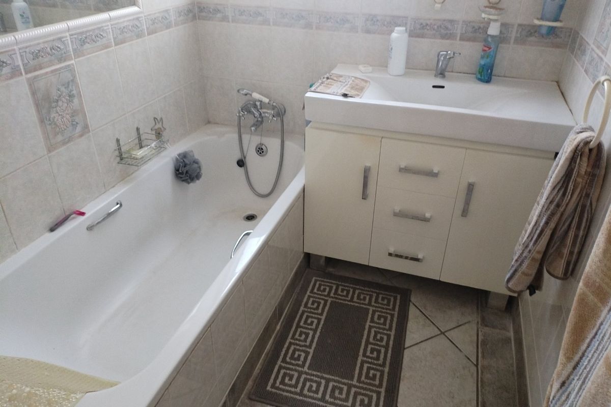 A functional bathroom featuring a built-in vanity with a ceramic basin, a standard bathtub with a handheld shower attachment, and neutral wall and floor tiling.