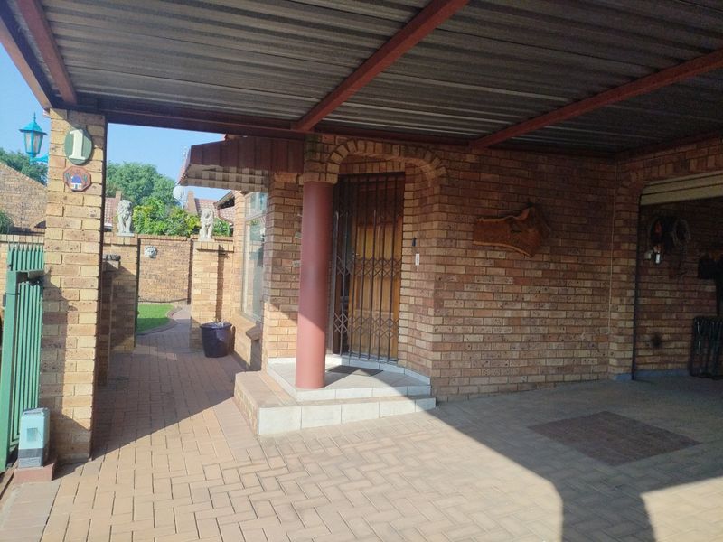 Front entrance of the townhouse featuring a covered carport, brick facade, and paved walkway leading to the main security gate.