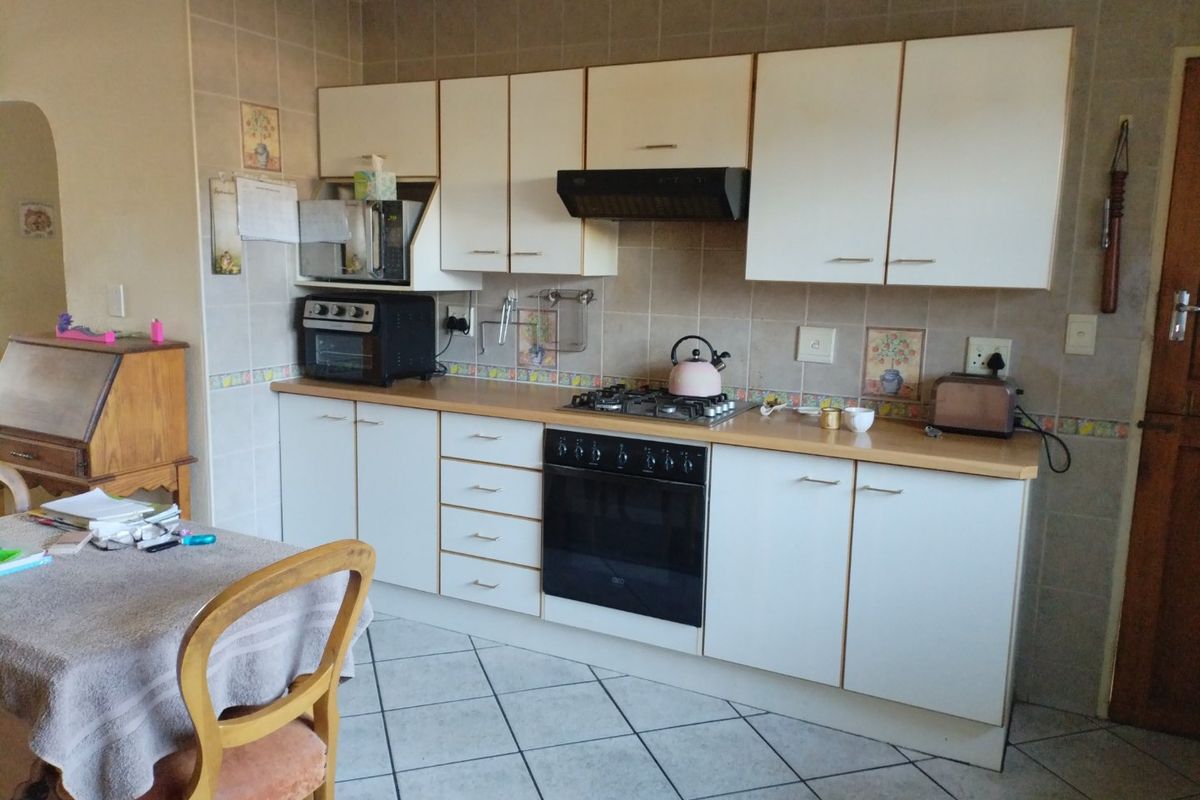 A functional kitchen featuring white cabinetry, a gas hob, built-in oven, extractor fan, and tiled splashback with neutral floor tiles.