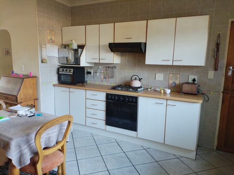 A functional kitchen featuring white cabinetry, a gas hob, built-in oven, extractor fan, and tiled splashback with neutral floor tiles.