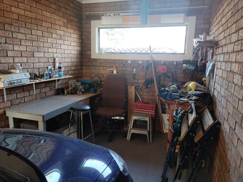A functional garage space featuring exposed brick walls, a horizontal window, and a built-in workbench, suitable for use as a workshop or storage area.