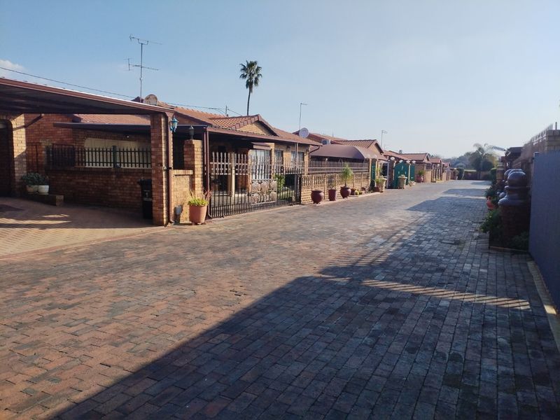A street-level view of a townhouse complex featuring brick-paved driveways, covered carports, and established brick-built residential units.