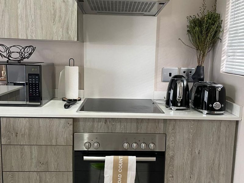 A modern kitchen featuring wood-grain cabinetry, stainless steel appliances including an oven and extractor fan, and a clean white stone countertop.