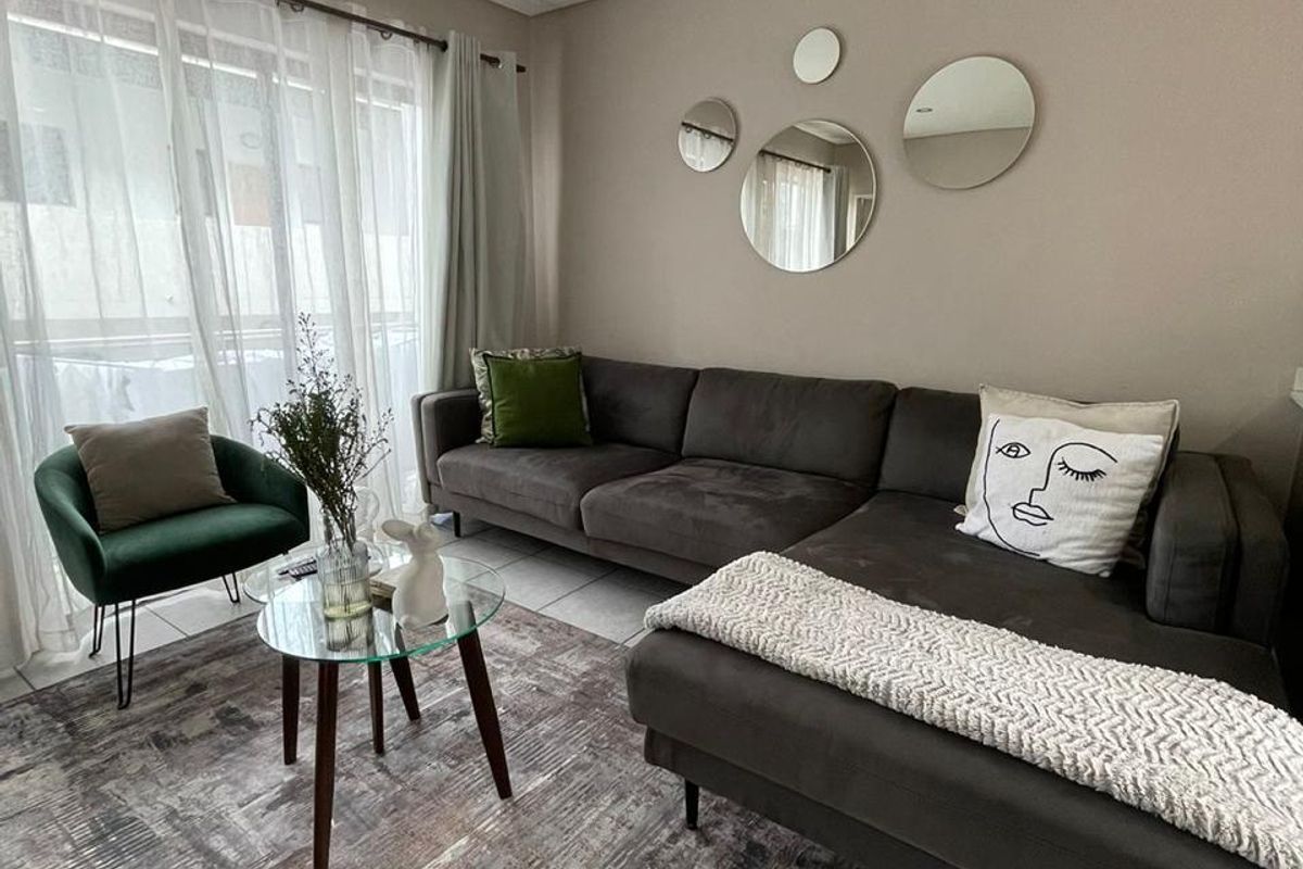 A well-maintained living room featuring neutral wall tones, tiled flooring, recessed lighting, and a large sliding glass door providing natural light.