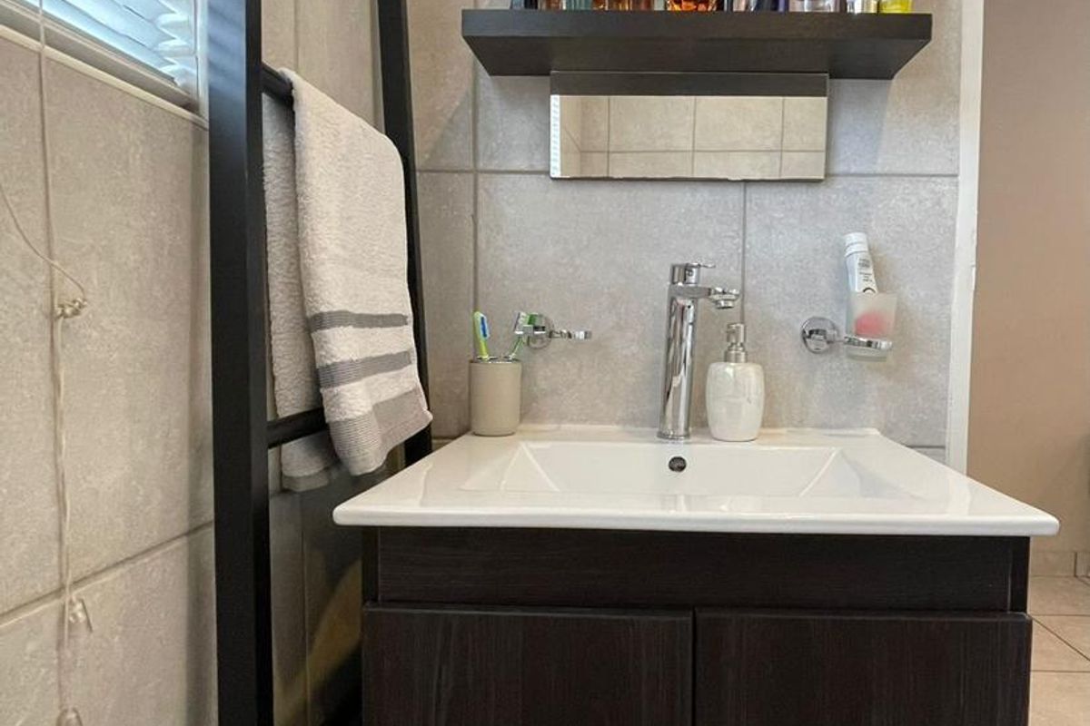 A functional bathroom featuring a modern dark wood vanity cabinet, ceramic basin with chrome mixer tap, wall-mounted mirror, and neutral wall tiling.