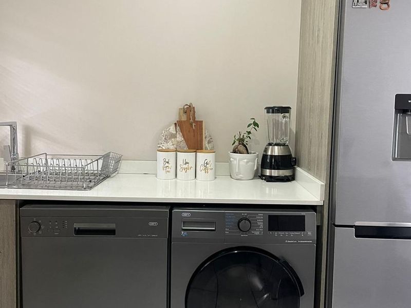 A functional laundry area featuring modern grey cabinetry, a clean countertop with a sink, and space for a dishwasher and washing machine.