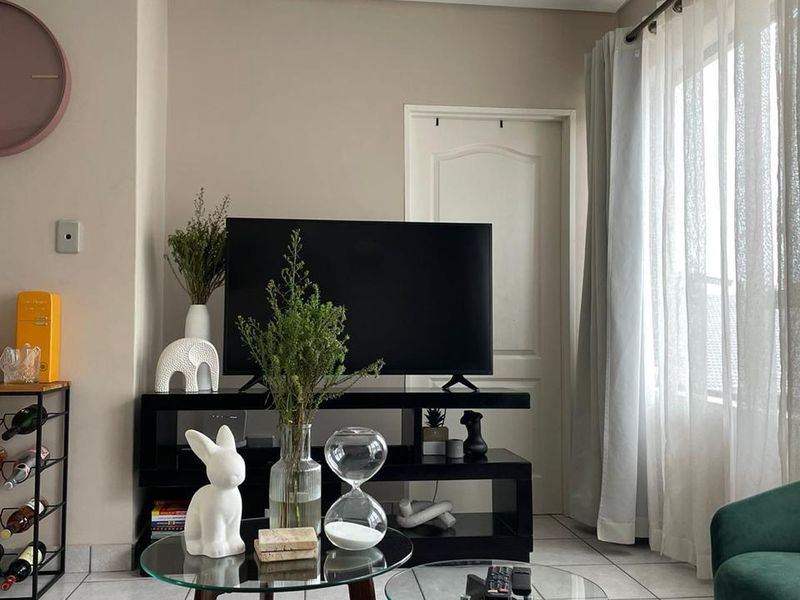 A well-maintained living room featuring neutral wall tones, tiled flooring, and natural light through large windows with curtain tracks.