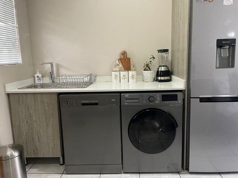 A functional laundry area featuring a stainless steel sink, stone countertop, and integrated cabinetry with space for a dishwasher and washing machine.