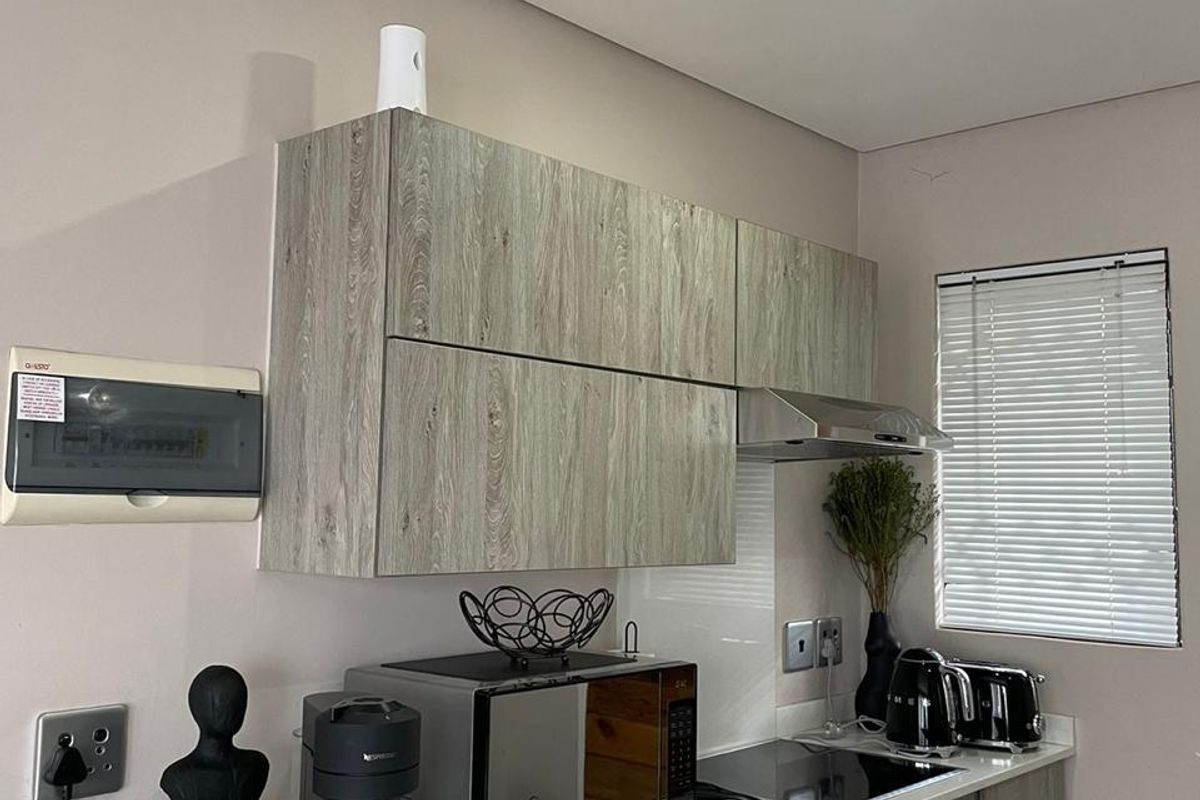 Modern kitchen featuring wood-grain cabinetry, stone countertops, integrated hob, oven, and extractor fan, complemented by neutral wall finishes and venetian blinds.