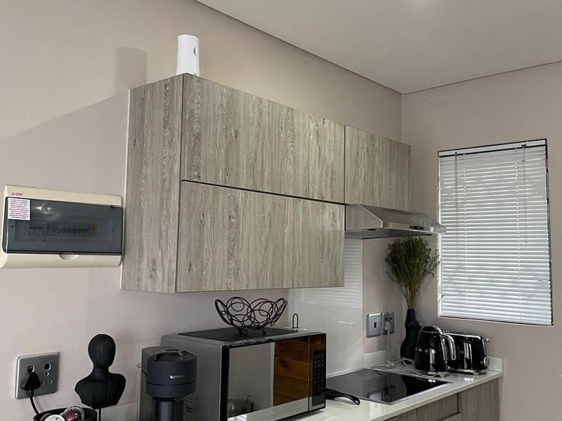 Modern kitchen featuring wood-grain cabinetry, stone countertops, integrated hob, oven, and extractor fan, complemented by neutral wall finishes and venetian blinds.