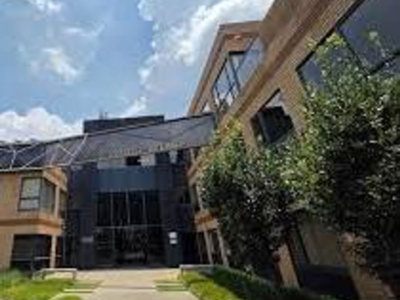 Front exterior view of a modern commercial office building featuring a brick facade, glass curtain walling, and a prominent metal entrance canopy.