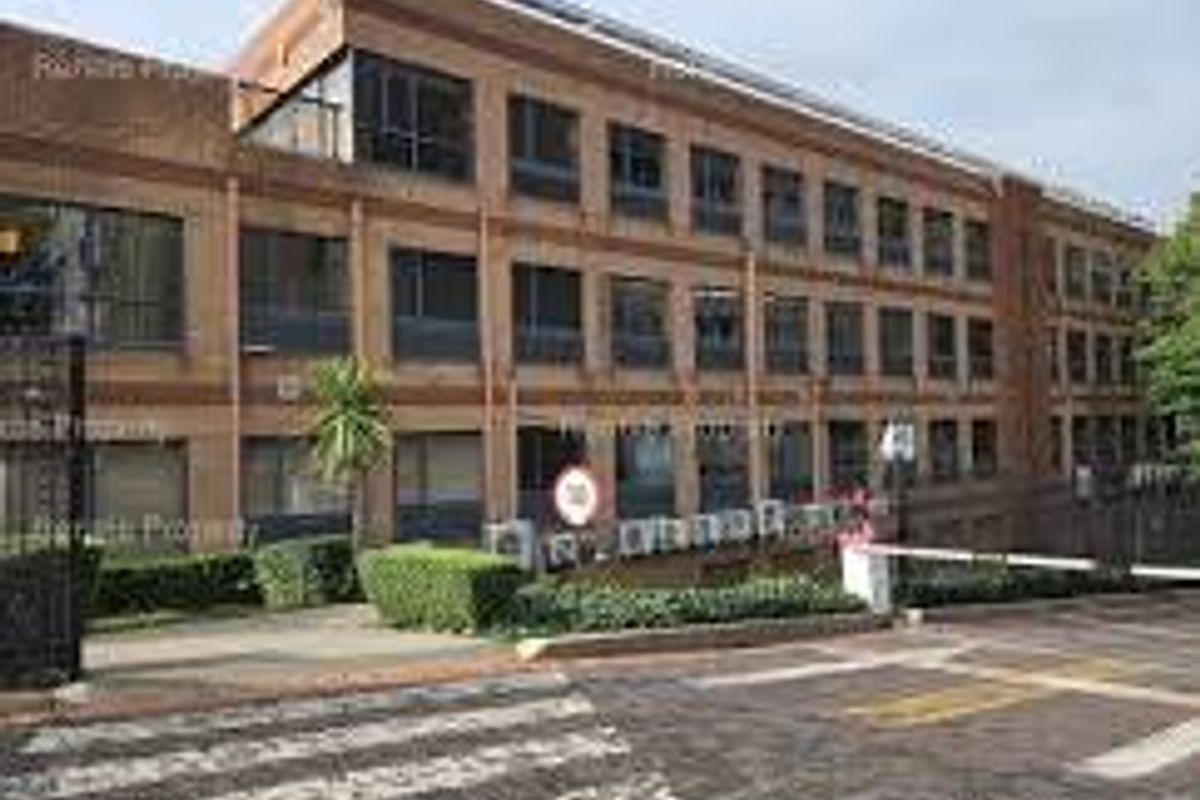 A multi-story commercial office building featuring a brick facade, large windows, and a secure gated entrance with paved driveway access.