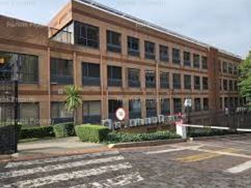 A multi-story commercial office building featuring a brick facade, large windows, and a secure gated entrance with paved driveway access.