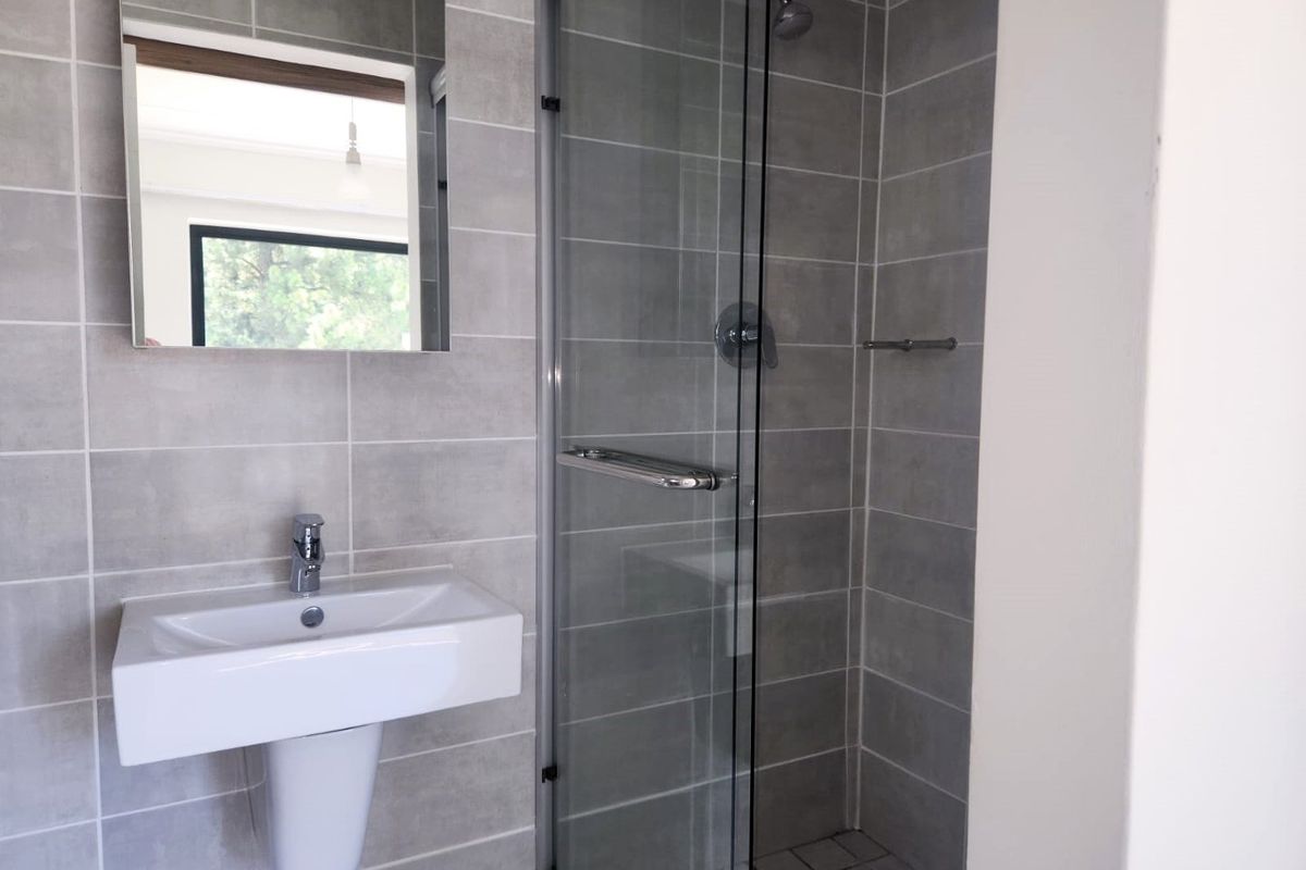 Modern bathroom featuring a pedestal washbasin, wall-mounted mirror, and a glass-enclosed shower with neutral grey wall tiling.