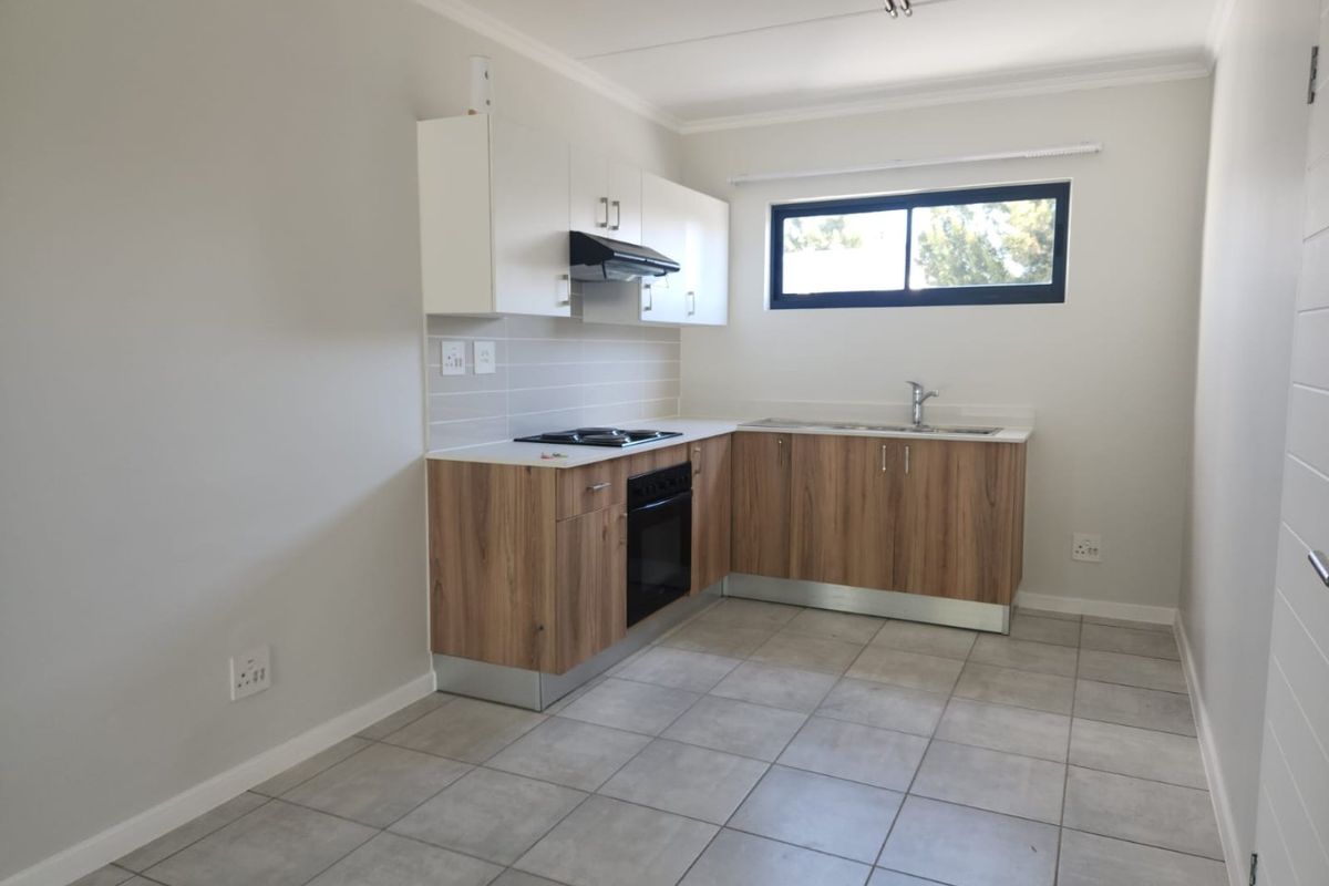 A clean, modern kitchen featuring wood-finish lower cabinets, white upper cabinetry, integrated appliances, and neutral tiled flooring in an open-plan layout.