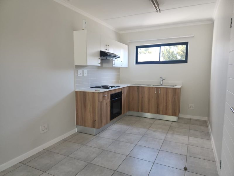 A clean, modern kitchen featuring wood-finish lower cabinets, white upper cabinetry, integrated appliances, and neutral tiled flooring in an open-plan layout.