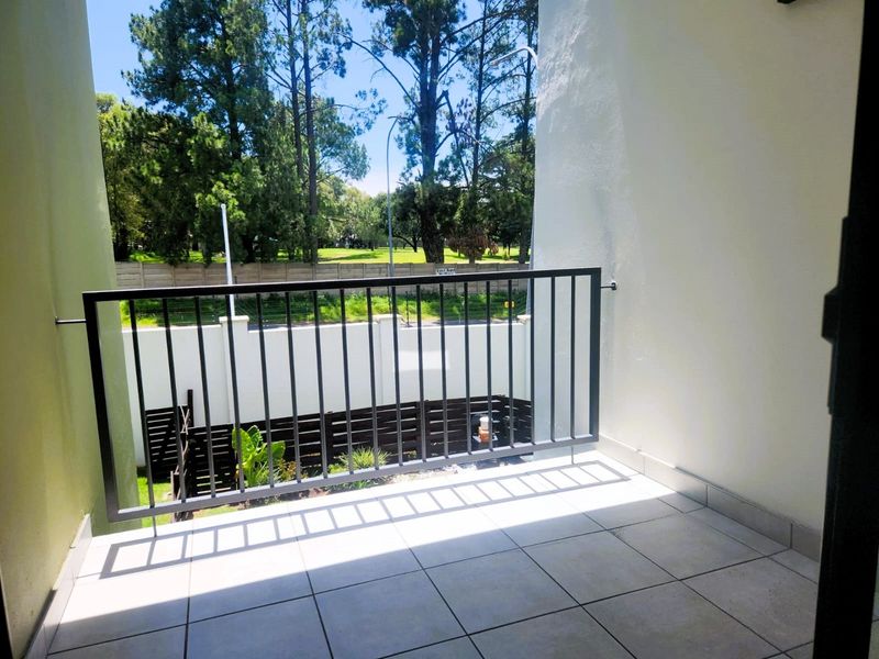 A clean, tiled balcony featuring a modern metal balustrade, offering an open view of the surrounding greenery and boundary wall.