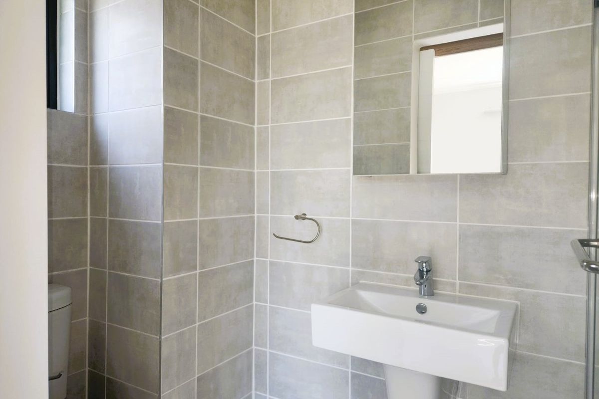Modern bathroom featuring neutral wall tiles, a pedestal washbasin with chrome fixtures, a wall-mounted mirror, and a glass-enclosed shower area.