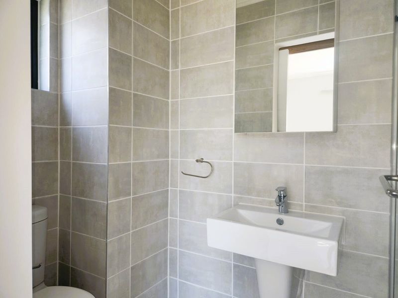 Modern bathroom featuring neutral wall tiles, a pedestal washbasin with chrome fixtures, a wall-mounted mirror, and a glass-enclosed shower area.