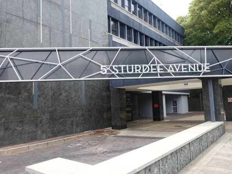 Front entrance view of a commercial building at 5 Sturdee Avenue, featuring modern stone cladding, metal signage, and a covered driveway approach.