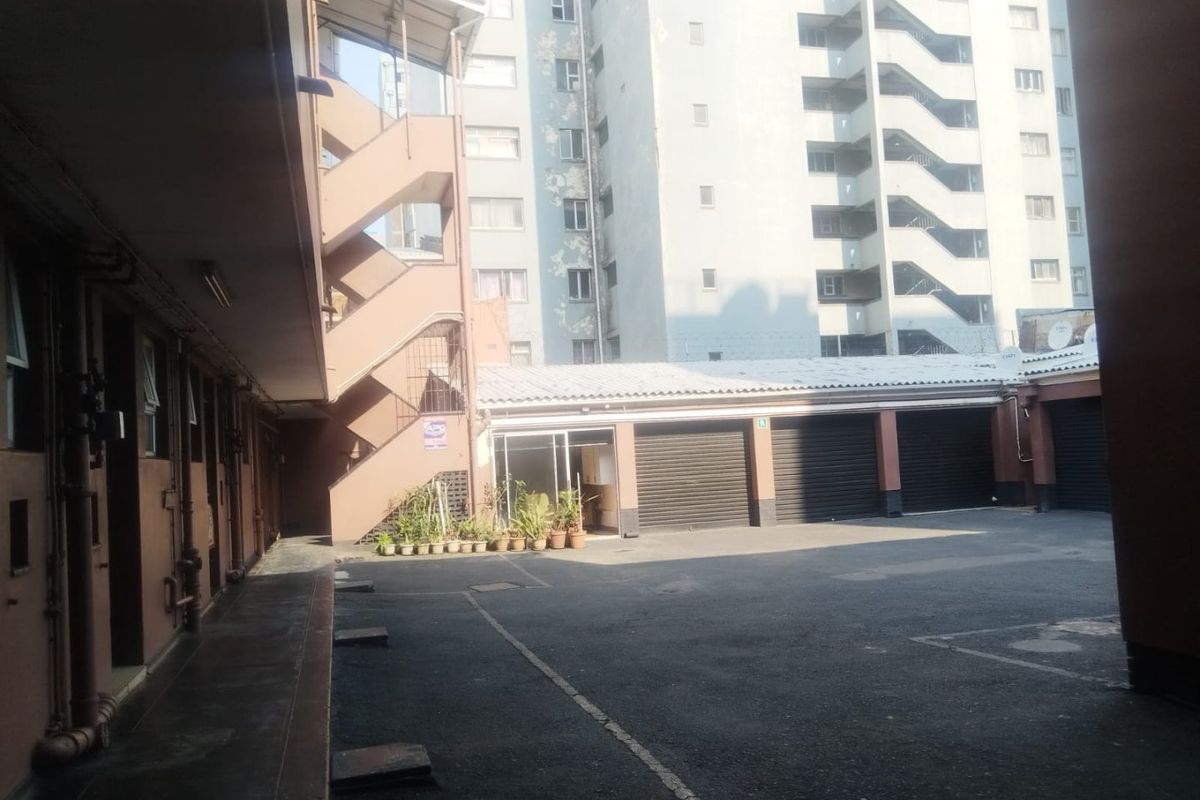 Rear courtyard area featuring a concrete staircase, multiple roller shutter garage doors, and access to the apartment building complex.