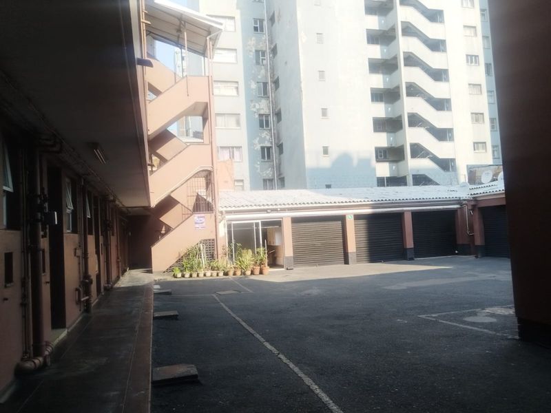 Rear courtyard area featuring a concrete staircase, multiple roller shutter garage doors, and access to the apartment building complex.