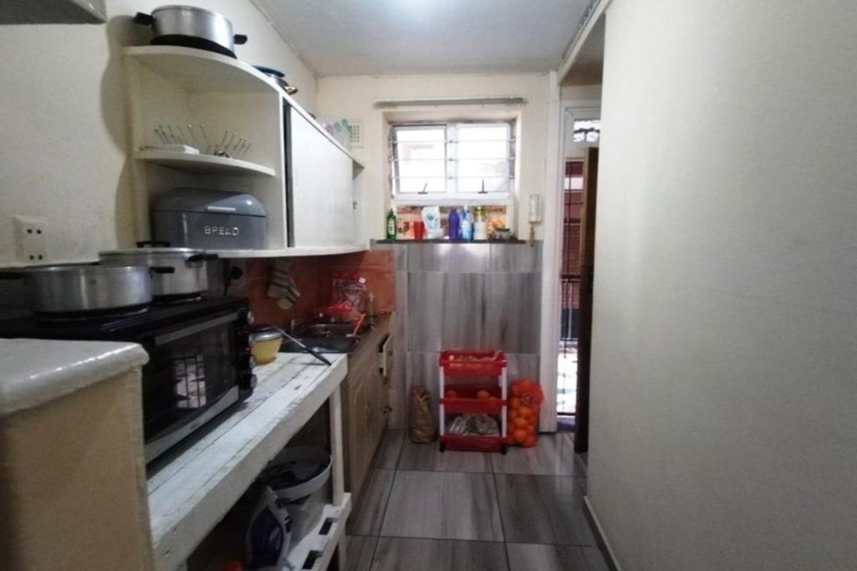 A compact kitchen featuring built-in cabinetry, tiled splashbacks, and tiled flooring, offering a functional layout in need of cosmetic updates.