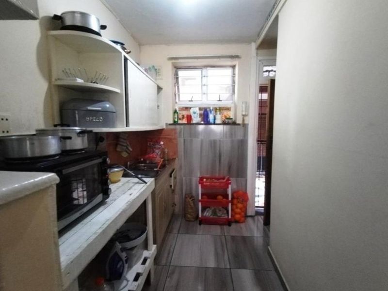 A compact kitchen featuring built-in cabinetry, tiled splashbacks, and tiled flooring, offering a functional layout in need of cosmetic updates.