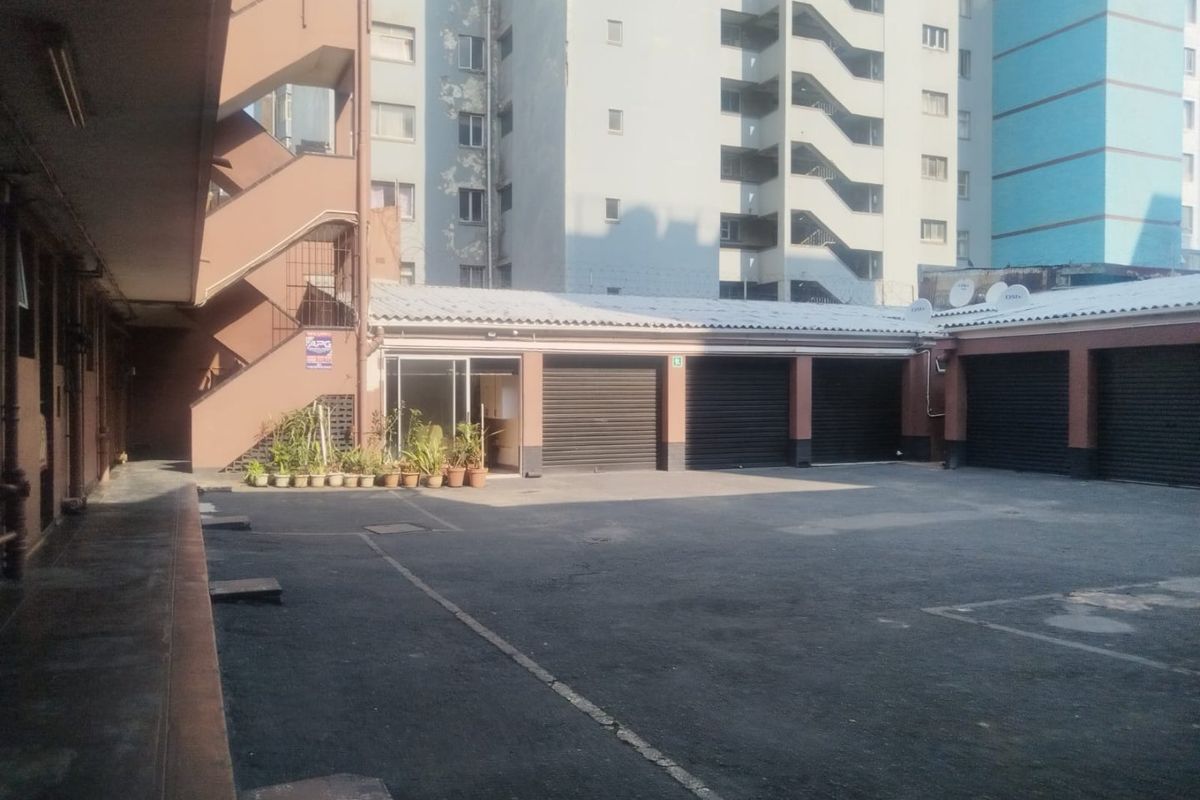 A paved courtyard area featuring multiple garage units with roller shutter doors and an external staircase leading to upper levels.